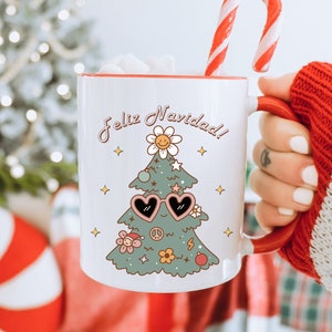 May include: White ceramic mug with a red rim and handle. The mug features a cartoon Christmas tree wearing sunglasses and the text "Feliz Navidad!" in Spanish.