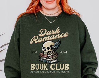 Peut inclure: Un sweat-shirt vert foncé avec le texte "Dark Romance Book Club" dans une police de caractères de style vintage. Le design présente un crâne tenant une plume et une pile de livres. Le texte "EST. 2024" et "Always Falling for the Villain" sont également inclus.