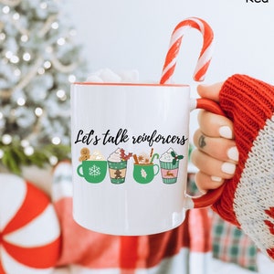 May include: White ceramic mug with a red rim and handle. The mug has a green and brown illustration of five holiday-themed mugs with the text "Let's talk reinforcers".