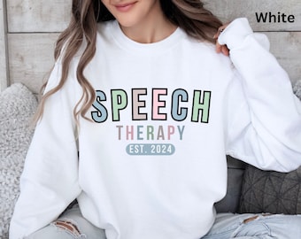 May include: White sweatshirt with the words "SPEECH THERAPY" in pastel colors. Below the text is "EST. 2024". The sweatshirt is a crew neck style and is being worn by a person.