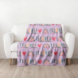 May include: A purple fleece blanket with a repeating pattern of rainbows, hearts, and the text "TEACHER" with the name "Mrs. Johnson".