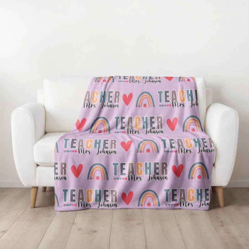 May include: A purple fleece blanket with a repeating pattern of rainbows, hearts, and the text "TEACHER" with the name "Mrs. Johnson".
