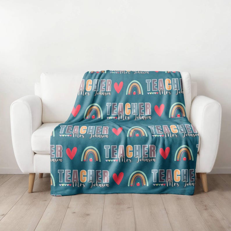 May include: A teal blue fleece blanket with a repeating pattern of rainbows, hearts, and the text "TEACHER Mrs. Johnson".