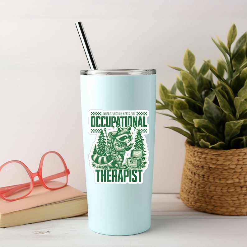 May include: A light blue tumbler with a green sticker featuring a raccoon with a backpack and a treasure chest. The sticker says "Where function meets fun for Occupational Therapist".