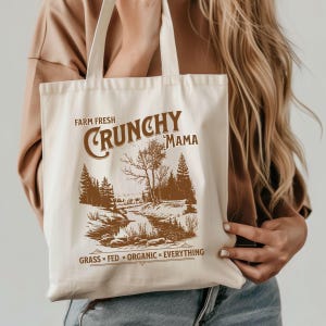 May include: A white canvas tote bag with brown text and a graphic design. The text reads "Farm Fresh Crunchy Mama" and "Grass Fed * Organic * Everything".