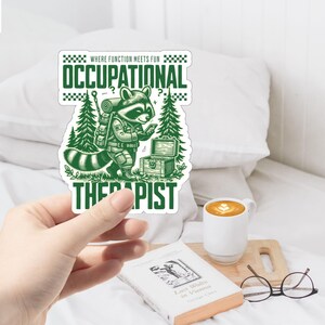 May include: Green and white sticker with a raccoon wearing a backpack and holding a phone. The text on the sticker reads "Where function meets fun Occupational Therapist".