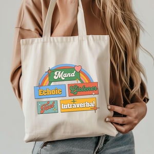 Könnte beinhalten: Cremefarbene Tragetasche mit Retro-Design. Sie zeigt die Wörter "Mand", "Echoic", "Listener", "Tact" und "Intraverbal" in farbenfrohem, stilisiertem Text sowie eine Regenbogen- und Herzgrafik. Die Tasche hat zwei Griffe.