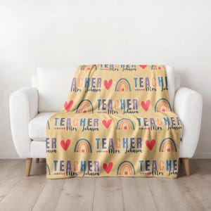 May include: A yellow fleece blanket with a repeating pattern of rainbows, hearts, and the text "TEACHER Mrs. Johnson".