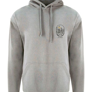 K&ouml;nnte beinhalten: Ein grauer Kapuzenpullover mit einem kleinen Schwarzwei&szlig;-Motiv eines Hauses mit einer Mondsichel und B&auml;umen. Das Motiv befindet sich in einem Kreis mit dem Wort "HOME" darunter.