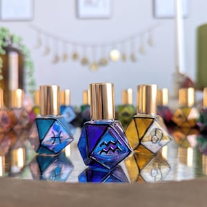 May include: A collection of colorful, geometric-shaped perfume bottles with gold-colored caps. Each bottle features a different zodiac symbol. The bottles are arranged on a reflective surface, with a blurred background.