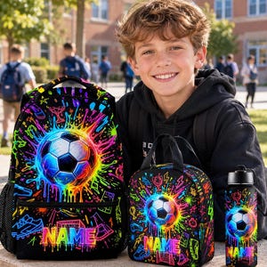 Könnte beinhalten: Ein Set aus schwarzem Rucksack, Lunchtasche und Trinkflasche mit einem leuchtend bunten Neon-Farbspritzer-Design, einer zentralen Fußballgrafik und dem Wort NAME in kräftigen, bunten Buchstaben auf jedem der drei Gegenstände.