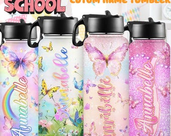 May include: Four cylindrical tumblers with black lids and handles, each featuring the name Annabelle in cursive script. Designs include butterflies, rainbows, floral patterns, and glitter finishes in pink, purple, and blue hues with Back to School text.