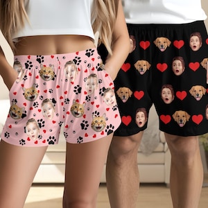 Puede incluir: Un par de pantalones cortos rosa y negro con un patrón de huellas de patas y corazones. Los pantalones cortos presentan varias caras de personas y animales. Un par de pantalones cortos negros a juego con un patrón de corazones y varias caras de personas y animales.