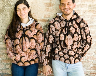 Peut inclure: Deux personnes portant des sweats à capuche noirs avec un motif de nombreux visages. Les sweats à capuche ont un cordon de serrage et une poche kangourou. Les personnes sont debout devant un mur de briques.