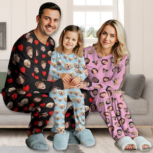 Könnte beinhalten: Passende Familienpyjamas. Die Erwachsenenpyjamas sind schwarz mit roten Herzen und Gesichtern. Die Kinderpyjamas sind hellblau mit Hunde-Gesichtern. Die anderen Erwachsenenpyjamas sind rosa mit Gesichtern.