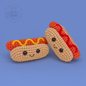 May include: Two crocheted hot dogs with smiling faces. One has yellow mustard, the other has red ketchup. The buns are tan, the hot dogs are orange, and the condiments are red and yellow. The background is a solid blue.