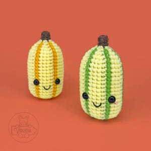 May include: Two crocheted plush toys shaped like fruits. One is yellow with orange stripes and the other is yellow with green stripes. Both have black eyes and a smiling mouth.