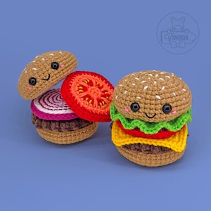 Könnte beinhalten: Gehäkelter Burger mit einem lächelnden Gesicht, Sesambrötchen, Salat, Tomate, Käse und einem braunen Patty. Der Burger ist aus Garn gefertigt und hat ein niedliches, cartoonartiges Design. Der Burger befindet sich auf blauem Hintergrund.