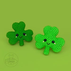 Può includere: Due foglie di trifoglio all'uncinetto verdi con facce sorridenti. I trifogli hanno occhi neri e guance bianche.