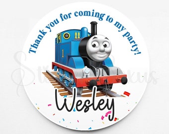 May include: Round thank you sticker with a blue and red cartoon train on a track. The text "Thank you for coming to my party!" is in blue text around the train. The name "Wesley" is written in black cursive below the train. The background is white with colorful confetti.