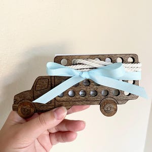 May include: Wooden toy truck with a light blue ribbon and white rope. The truck has holes in the back and the words "ARE the hands wash the soap" are visible.