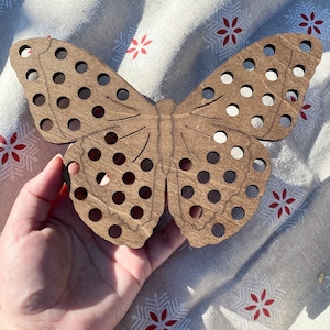 May include: A wooden butterfly-shaped craft with holes for threading yarn or string. The butterfly is brown and has a natural wood finish.