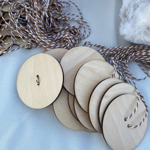 May include: A collection of unfinished wooden circle ornaments with pre-drilled holes for stringing. Each ornament is approximately 3 inches in diameter and has a natural wood grain. Twine with brown and white strands is included.