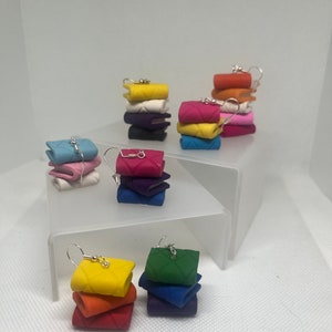 May include: A set of colorful polymer clay earrings shaped like stacks of books. Each stack has a different color scheme, including yellow, orange, red, green, blue, purple, pink, and white.