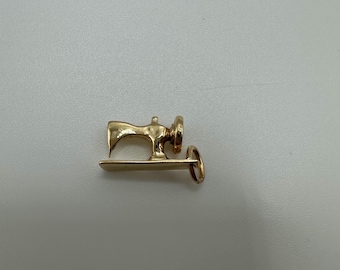 May include: A gold-colored sewing machine charm with a loop for attaching to a necklace or bracelet.