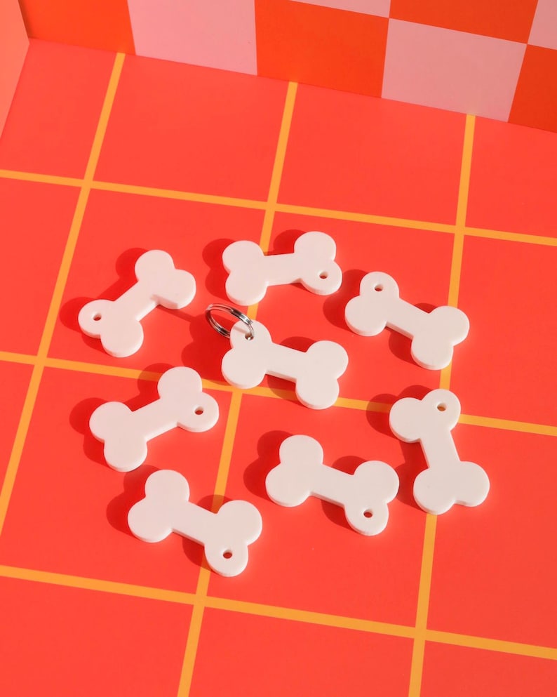 May include: Eight white bone-shaped dog tags on a red and orange checkered background. The tags have a hole at each end.