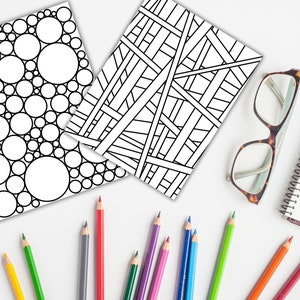 May include: Two black and white coloring pages, one with a pattern of overlapping circles and the other with a geometric pattern of intersecting lines.  A set of colored pencils and a pair of glasses are also in the image.