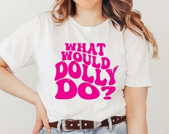 May include: A white short-sleeved t-shirt featuring the hot pink text WHAT WOULD DOLLY DO? in a bold, wavy font. The shirt is paired with light blue denim jeans, a brown leather belt with a silver buckle, and an orange felt cowboy hat.