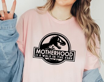 May include: A pink t-shirt with a black graphic of a dinosaur and the text "Motherhood is a walk in the park".