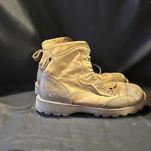 May include: A pair of tan-colored combat boots with laces and a high-top design. The boots show signs of wear and tear, with visible scuffs and dirt. The soles are thick and rugged, suitable for outdoor activities.