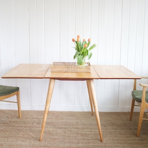 May include: A wooden dining table with a drop leaf extension, two chairs with green cushions, and a vase of orange tulips on the table.