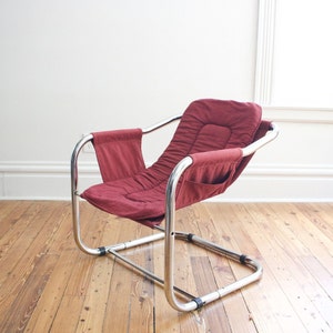 May include: A red upholstered chair with a chrome frame. The chair has a unique design with a curved back and a wide seat.