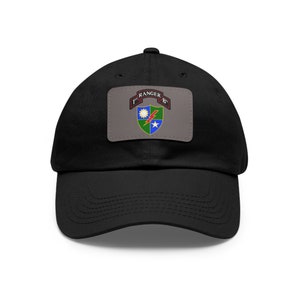 May include: Black baseball cap with a gray patch featuring the text "1st RANGER B" and a colorful emblem. The emblem includes a sun, lightning bolt, star, and shield design. A classic, adjustable hat.