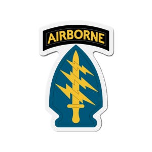 May include: A die-cut sticker featuring a black tab at the top with the word AIRBORNE in yellow letters. Below is a blue shield-shaped emblem containing a yellow vertical dagger overlaid with three yellow lightning bolts pointing to the right.