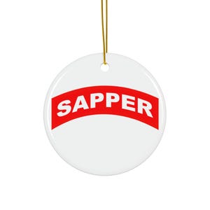 May include: White ceramic ornament with a red curved banner that says "SAPPER" in white letters.