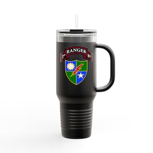 Può includere: Tazza da viaggio nera con manico e cannuccia. La tazza presenta un emblema colorato con la scritta "2D RANGER BN". L'emblema include un sole, un fulmine e una stella su uno scudo. La tazza è progettata per mantenere le bevande calde o fredde.