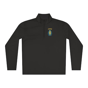 Puede incluir: Jersey negro de manga larga con cuello con cremallera de un cuarto. La camisa presenta un parche en la parte superior del pecho con la palabra "AIRBORNE" encima de un emblema azul y amarillo. El emblema representa un árbol con rayos.