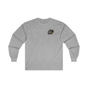 Könnte beinhalten: Ein graues Langarmshirt mit einem gestickten Logo in Schwarz und Gold eines Maskottchens auf der linken Brust. Das Maskottchen ist ein schwarzer Bär mit einem goldenen Helm und einem goldenen Buchstaben "A" auf der Brust.