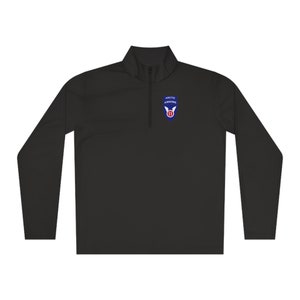 May include: Black long-sleeve performance shirt with a quarter zip closure. The shirt features a blue and white patch with the text "ARCTIC AIRBORNE" and a red number "11" inside a white wing.