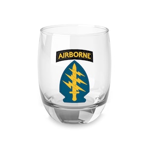 Puede incluir: Un vaso transparente de vidrio con un gráfico azul y dorado del emblema de las Fuerzas Especiales Aerotransportadas. El gráfico incluye las palabras "AIRBORNE" en amarillo.