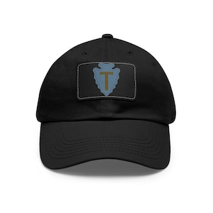 May include: A black baseball cap with a patch featuring a blue arrowhead with a gold "T" inside. The patch is surrounded by a white border.