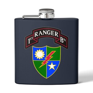 Può includere: Una fiaschetta blu navy con tappo e cerniera argentati. La fiaschetta presenta uno stemma con la scritta "1st Ranger Bn" in bianco su uno stendardo rosso. Lo stemma include anche un sole, un fulmine e una stella.