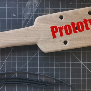 May include: A wooden paddle with a black leather strap and tassel. The paddle has multiple holes drilled into it and the word "Prototype" is printed in red letters.