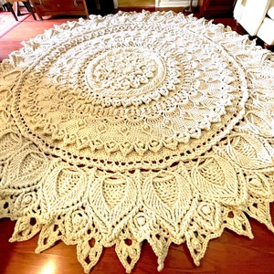 K&ouml;nnte beinhalten: Ein gro&szlig;er, runder, cremefarbener H&auml;kelteppich mit einem detaillierten Mandala-Muster. Der Teppich hat eine zarte, spitzenartige Textur und ist aus dickem Garn gefertigt.