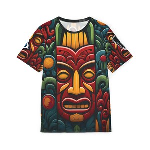 May include: A colorful t-shirt with a large, detailed tiki mask design. The mask is red, yellow, and orange with black eyes and a wide, open mouth. The background is a dark green with intricate patterns.