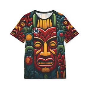 May include: A colorful t-shirt with a large, detailed tiki mask design. The mask is red, yellow, and orange with a black outline. The background is a dark green with floral patterns. The shirt has a short sleeve and a crew neck.